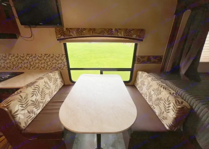 RV rental interior: dinette with patterned cushions, table, and window showing green grass. Features TV and kitchenette.. Jayco Jay Feather Ultra Lite 2015