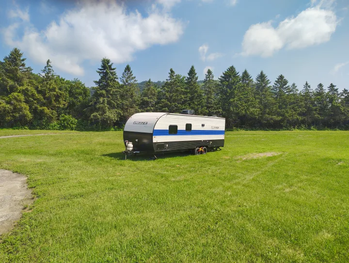 This white and blue Clipper travel trailer, an ideal rv rental for outdoor adventures, sits in a sunny grassy field.. Coachmen Clipper 26BH 2024