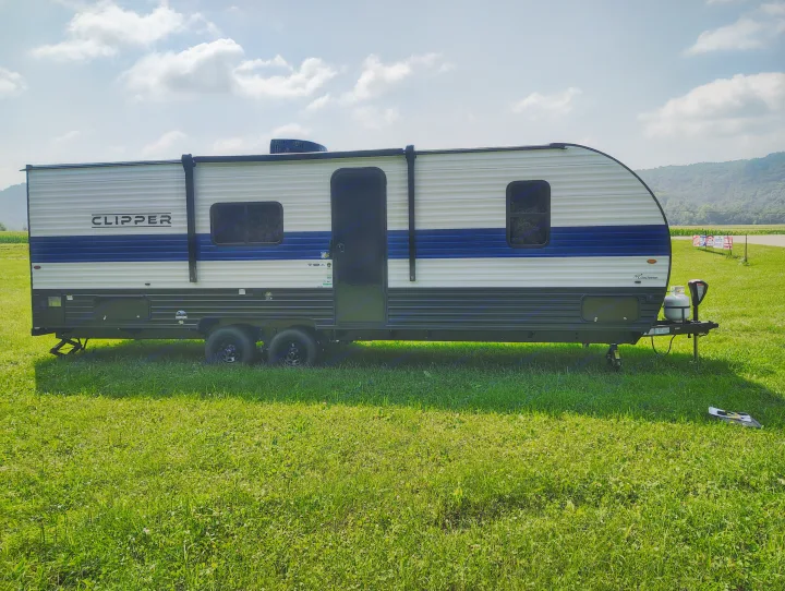 White and blue Clipper travel trailer rv rental on green grass, set against a backdrop of mountains. Ready for adventure!. Coachmen Clipper 26BH 2024