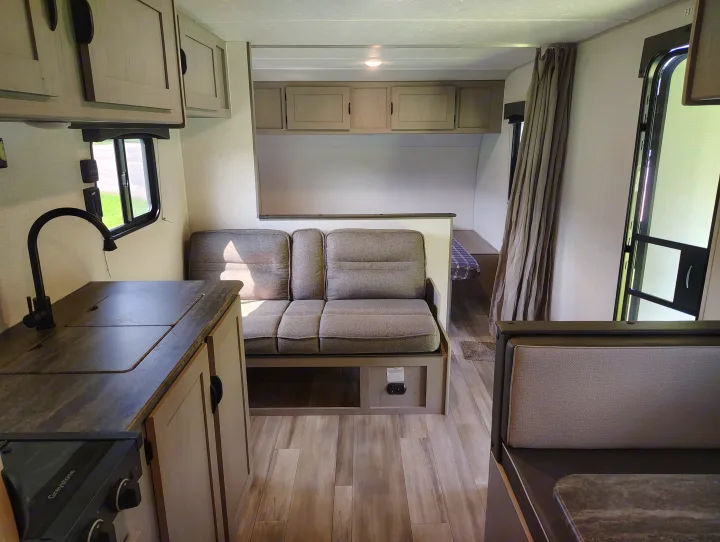 RV rental interior: A compact kitchen, comfortable sofa, and a partial view of a bed and dinette, offering a cozy travel space.. Coachmen Clipper 26BH 2024