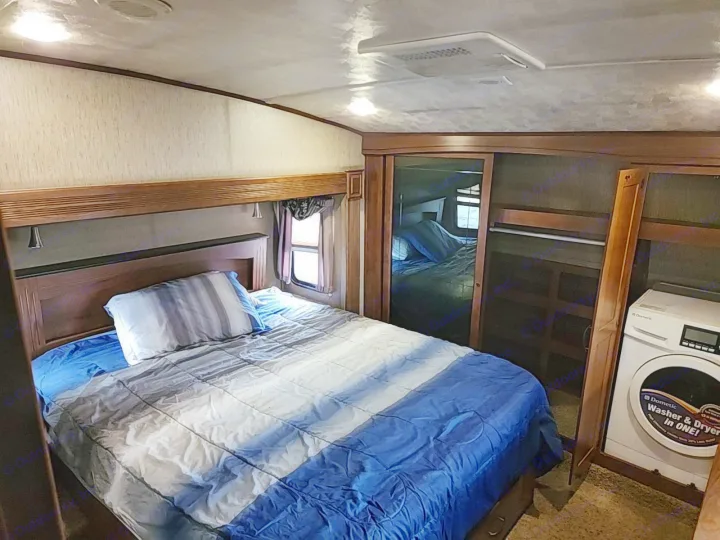 Comfortable RV rental bedroom with a striped bedspread, mirrored closet, and a Dometic washer/dryer. Enjoy travel amenities!. Forest River SABRE 2015