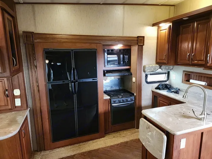 This RV rental offers a well-equipped kitchen featuring a black refrigerator, microwave, stove/oven, sink, and wooden cabinets.. Forest River SABRE 2015