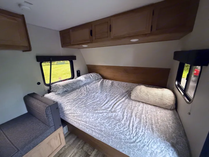 Inviting RV rental bedroom with a comfortable bed, overhead cabinets, and compact seating. Perfect for your next adventure.. Forest River Cherokee Wolf Pup 2024