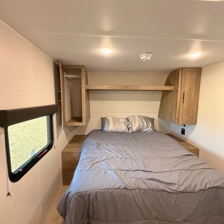 Step into this comfortable RV rental bedroom, featuring a large bed, built-in overhead storage, and a side window.. Keystone RV Springdale Mini 2026