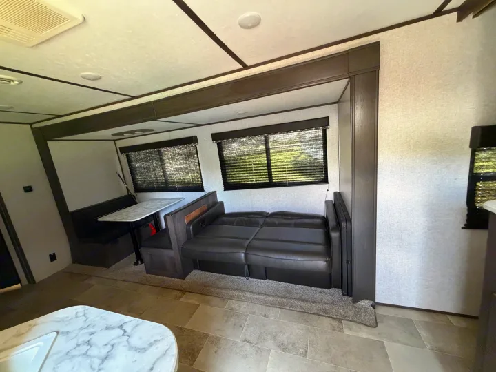 RV rental interior: A compact living area featuring a dinette, a comfortable sofa bed, and blinds on windows, with light walls and dark trim.. Dutchmen Coleman Lantern LT 2021