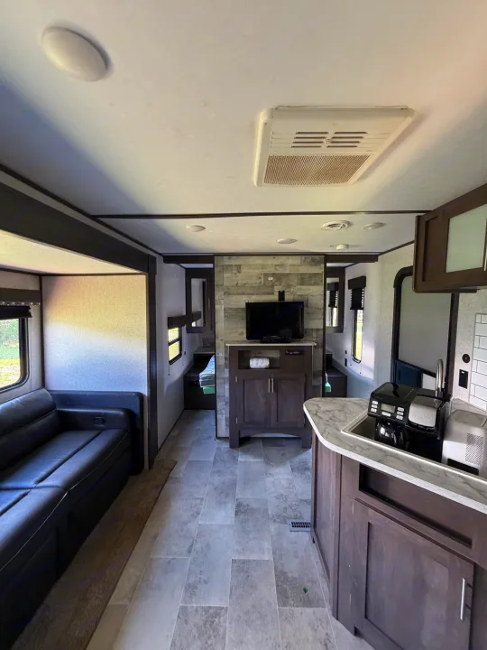 Modern RV rental interior: spacious living area with sofa, kitchen, and entertainment unit. Perfect for your next adventure!. Dutchmen Coleman Lantern LT 2021