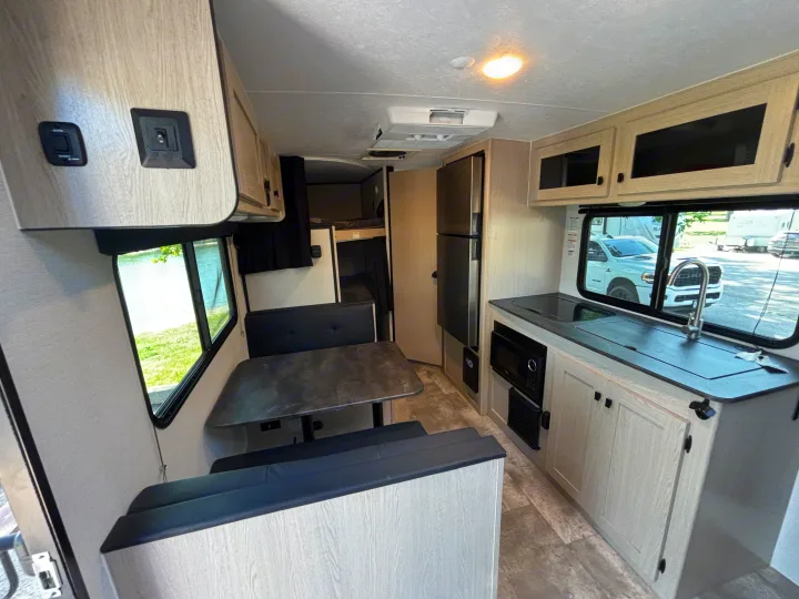 Inside a modern RV rental: light wood kitchen, dining booth, and bunk beds. Views outside from the windows.. Coachmen Apex Nano 2024