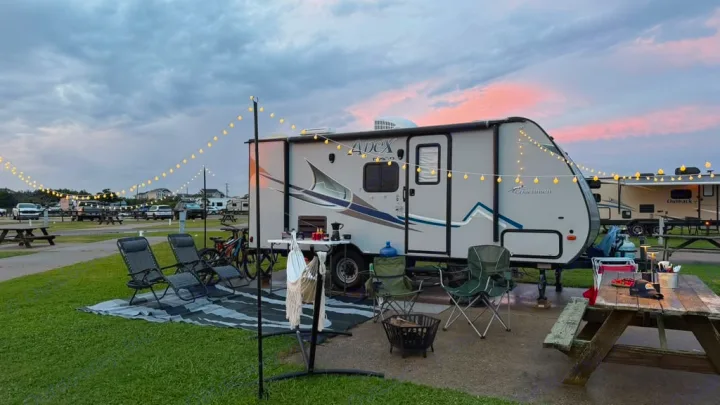 Inviting RV rental campsite with travel trailer, string lights, outdoor setup, and picnic table at sunset.. Coachmen Apex 2017