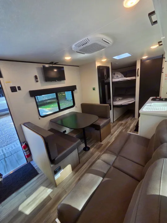 Bright rv rental interior featuring a dining booth, sofa, bunk beds, small kitchen area, and a wall-mounted TV.. Jayco Jay Flight SLX Sport Edition 2026