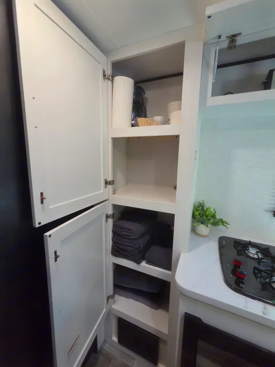 RV rental interior: open white cabinet with coffee maker, paper towels, cups, and folded towels next to a compact stove.. Jayco Jay Flight SLX Sport Edition 2026