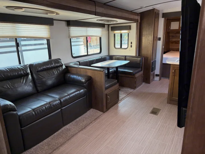 Modern RV rental living area with comfy leather sofa, U-shaped dinette, and light tile floor, bathed in natural light.. Keystone RV Passport GT 2021
