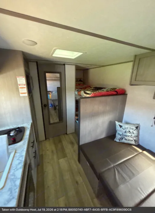 RV rental interior: compact kitchen, mirrored door, cozy bunk bed, and dinette with 'adventure' pillow. Ready for your trip!. Dutchmen Coleman Lantern LT 2023