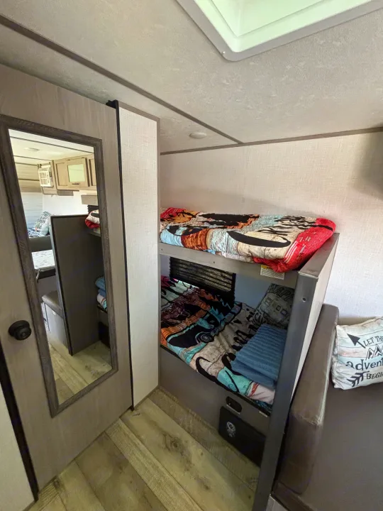 This RV rental interior showcases cozy bunk beds with colorful bedding and a compact living area, ideal for family travel.. Dutchmen Coleman Lantern LT 2023