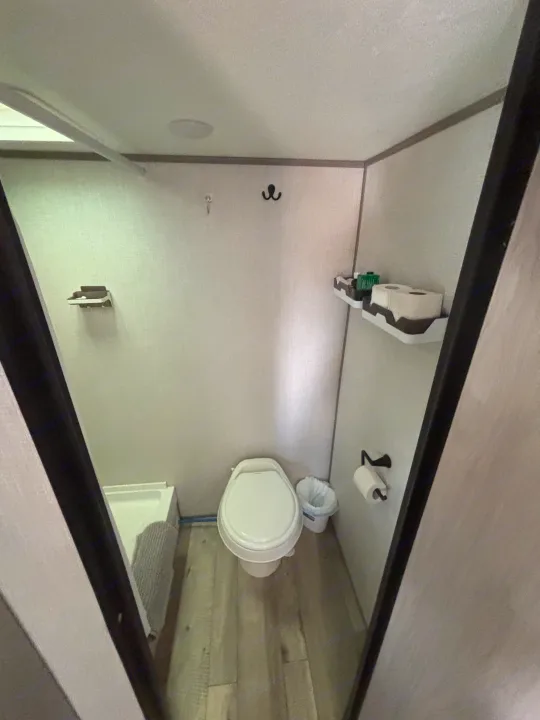 This compact RV rental bathroom includes a toilet, small shower area, wall shelves, and hooks for convenience.. Dutchmen Coleman Lantern LT 2023