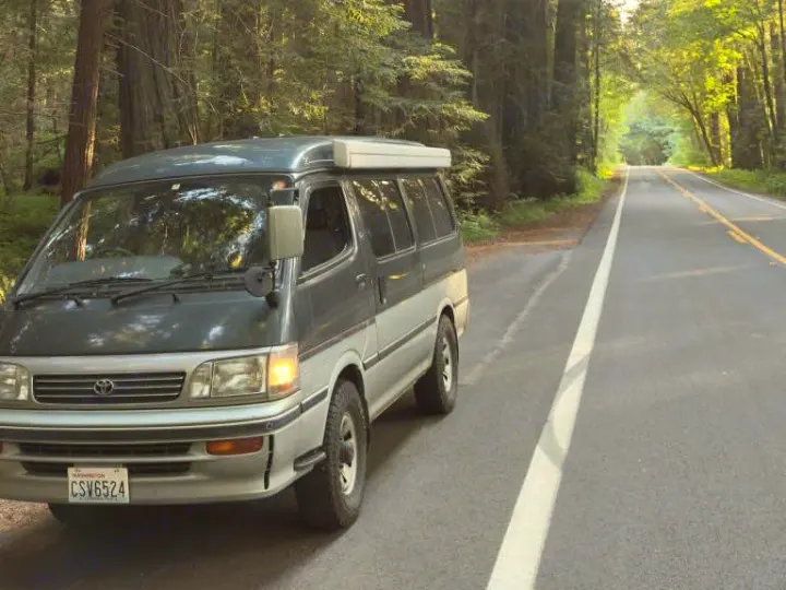 RV rental camper van parked on a scenic road through a beautiful forest, perfect for a Washington road trip.. Toyota Hiace Campervan 1994