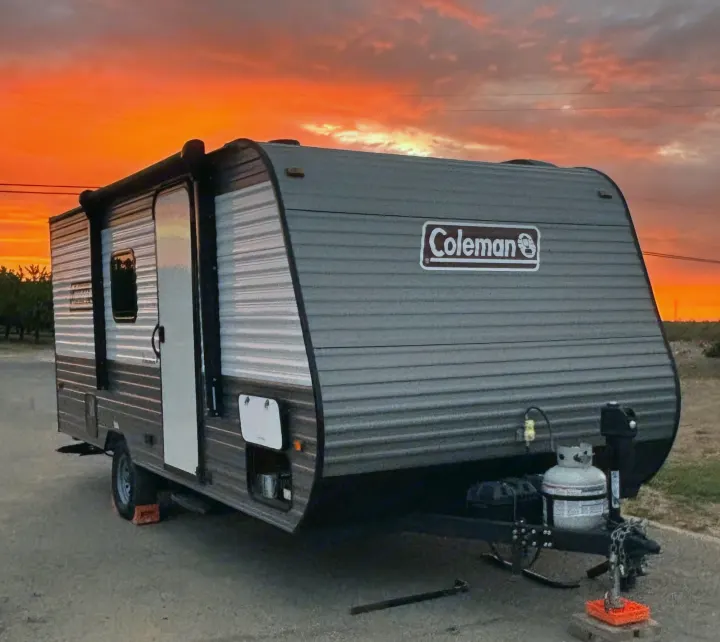 This RV rental, a Coleman travel trailer, is parked outdoors under a stunning orange sunset, ready for camping adventures.. Dutchmen Coleman Lantern LT 2023