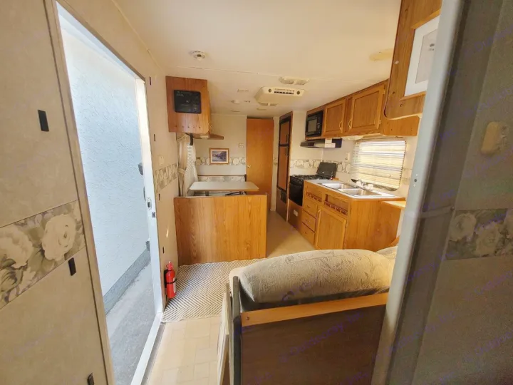 RV rental interior: A compact kitchen with wooden cabinets, sink, and stove, next to a dining booth. Ready for your trip.. Fleetwood 23T6 2004