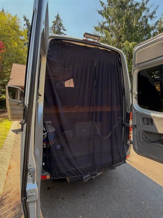 Rear view of an RV rental van with both doors open, revealing a black bug screen and gear inside, parked outdoors.. Mercedes Sprinter 2008