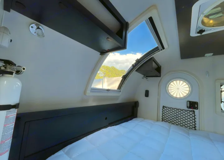 Cozy RV rental interior with a comfy bed, overhead storage, and open windows, offering a bright, airy feel in this camper.. nuCamp T@G 2022