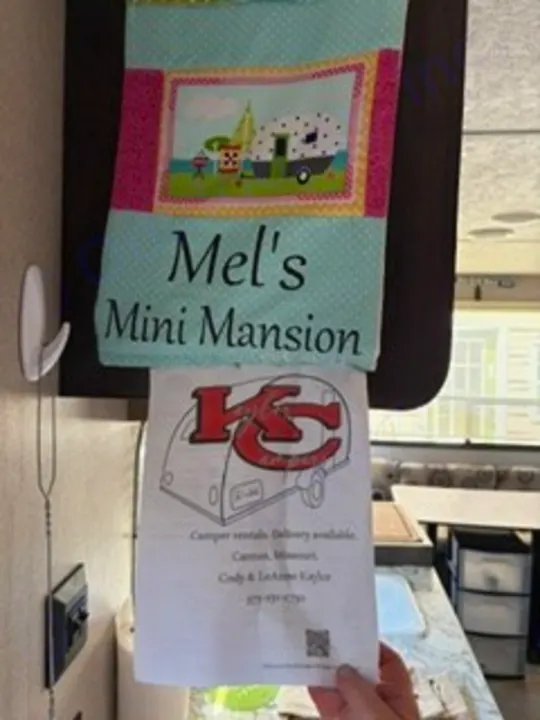 Hand holds "KC Kampers" rv rental flyer below "Mel's Mini Mansion" camper banner in RV interior.. Keystone RV Springdale Eco-Lite 2018