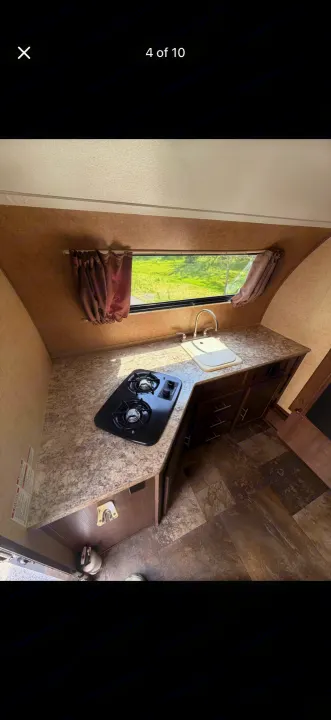 RV rental interior: A functional kitchen featuring a two-burner stove, sink, and window with curtains looking outside.. Forest River R-Pod 2016