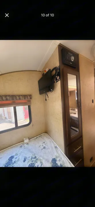 RV rental bedroom with bed, window, TV, and entertainment system above a mirrored wardrobe. Cozy travel space.. Forest River R-Pod 2016