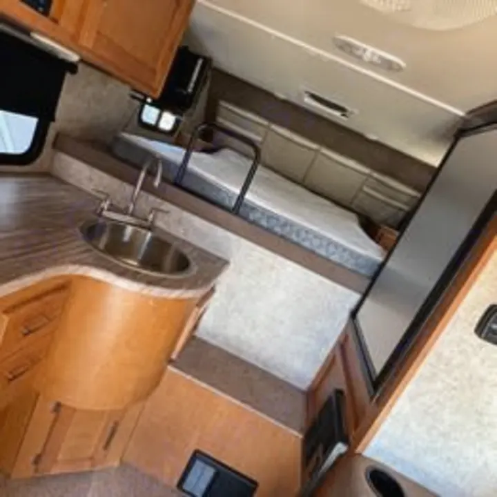 Interior view of an RV rental: a compact kitchenette with sink and a raised bed area. Perfect for camper adventures.. Adventurer/F150 ecoboost 80RB 2018