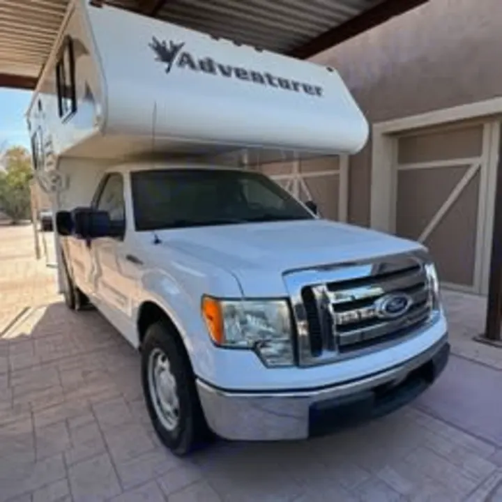 White Ford F-150 pickup with Adventurer truck camper, parked under cover. Ideal RV rental choice.. Adventurer/F150 ecoboost 80RB 2018