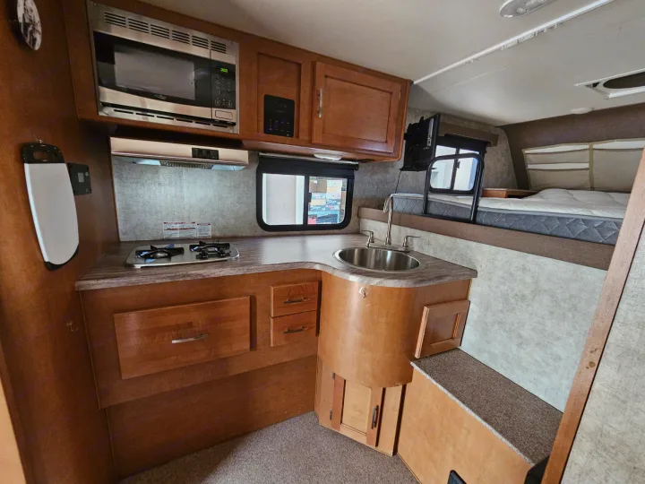 Inside an RV rental: functional kitchenette with microwave, stove, sink, and an overhead sleeping bunk for comfortable travel.. Adventurer/F150 ecoboost 80RB 2018