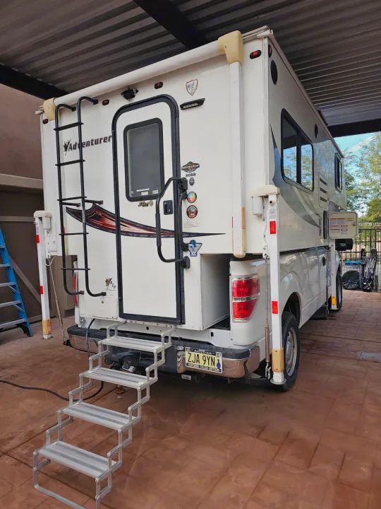 Rear of an Adventurer truck camper RV rental on a pickup, with stairs extended for easy access under a carport.. Adventurer/F150 ecoboost 80RB 2018