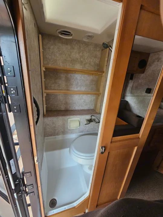 Inside an RV rental bathroom, featuring a compact toilet, shower, sink, and built-in shelves for efficient use of space.. Adventurer/F150 ecoboost 80RB 2018