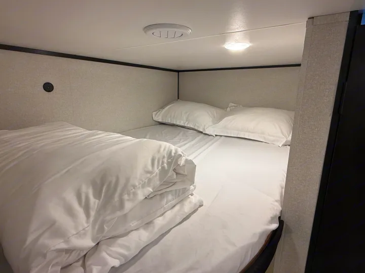 Cozy RV rental bunk bed with fresh white bedding, offering a compact sleeping area featuring a vent and light.. Heartland Powler 2026