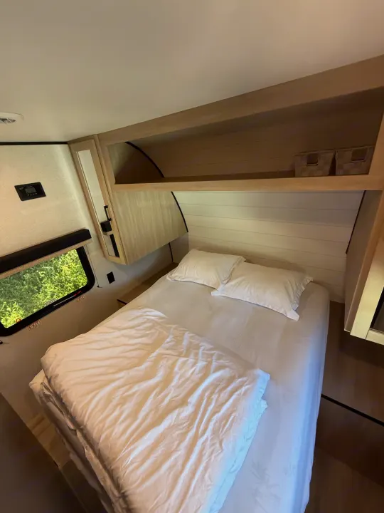 Explore this RV rental bedroom's cozy interior, featuring a comfortable bed, window with nature view, and overhead storage.. Heartland Powler 2026