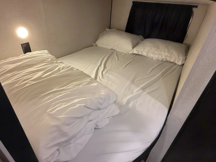 Cozy RV rental sleeping area features a comfortable bed with white bedding, pillows, and a personal reading light.. Heartland Powler 2026