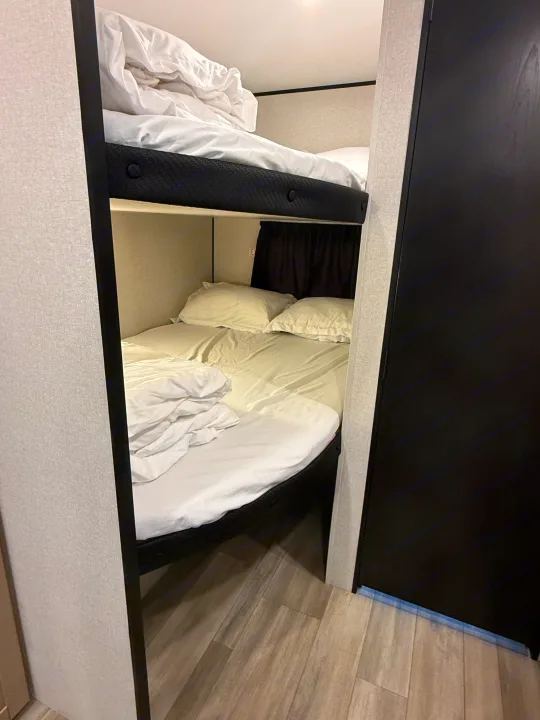 This RV rental features stacked bunk beds, made with crisp white sheets, a dark privacy curtain, and modern flooring.. Heartland Powler 2026