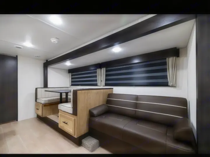 Cozy RV rental interior shows a U-shaped dinette, table, and brown sofa. Features window blinds for comfortable travel.. Forest River Cherokee Grey Wolf 2026