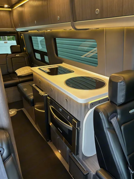 Inside a premium RV rental: modern kitchen with cooktop, microwave, and fridge, plus comfy leather seating.. Airstream Interstate 2021