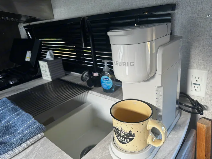 RV rental kitchen featuring a Keurig coffee maker, Glacier Park mug, sink, soap, and towels. Perfect for morning coffee.. Forest River Wildwood X-Lite 2021
