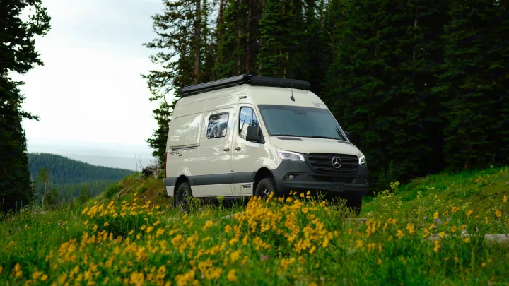 Winnebago Revel 4x4 RV rental amidst a mountain meadow of yellow flowers and pine trees, perfect for outdoor adventures.. Mercedes Winnebago 2024