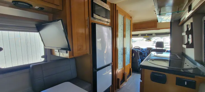 Inside an rv rental: compact kitchen with fridge, microwave, sink, and a dining booth with a TV mounted on the wall.. Coachmen Crossfit 2019