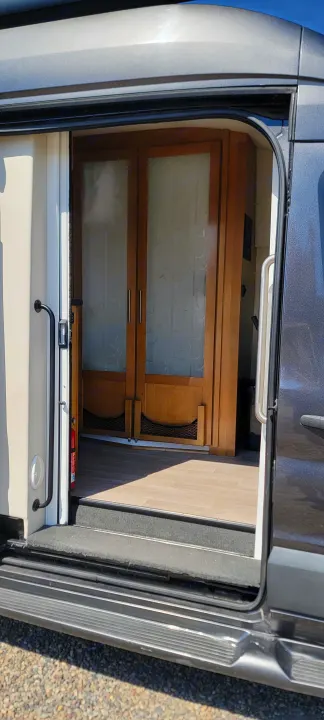 Open side door of an RV rental reveals a cozy interior with frosted wooden doors, grab handles, and step-in access.. Coachmen Crossfit 2019