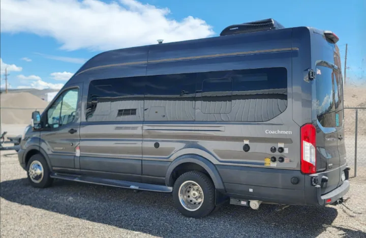 This dark grey Coachmen camper van, perfect for an RV rental, shows its Dometic roof AC and side utility hookups outdoors.. Coachmen Crossfit 2019