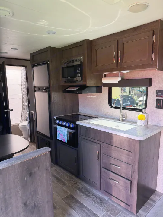 RV rental kitchen and dining area. Features dark wood cabinets, stove, microwave, sink, fridge, and cozy dinette.. Jayco Jay Flight SLX 2021