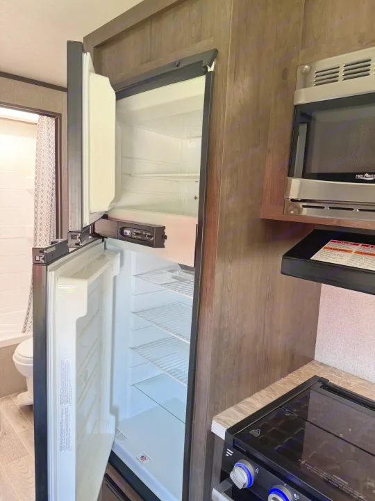 RV rental interior: Compact kitchen with open fridge, microwave, and stovetop, plus a peek into the bathroom.. Jayco Jay Flight SLX 2021