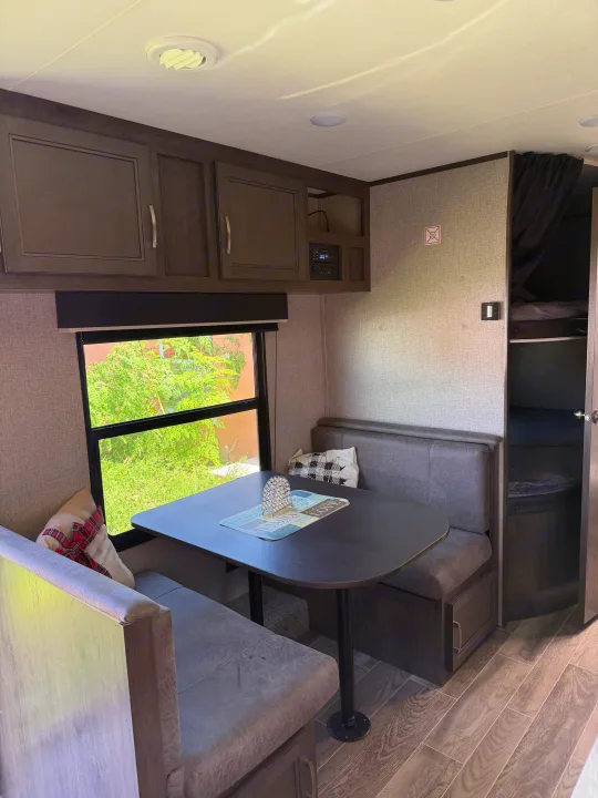 Inside a modern rv rental: dinette with table & bench seating, overhead cabinets, window view, and glimpse of bunk beds.. Jayco Jay Flight SLX 2021
