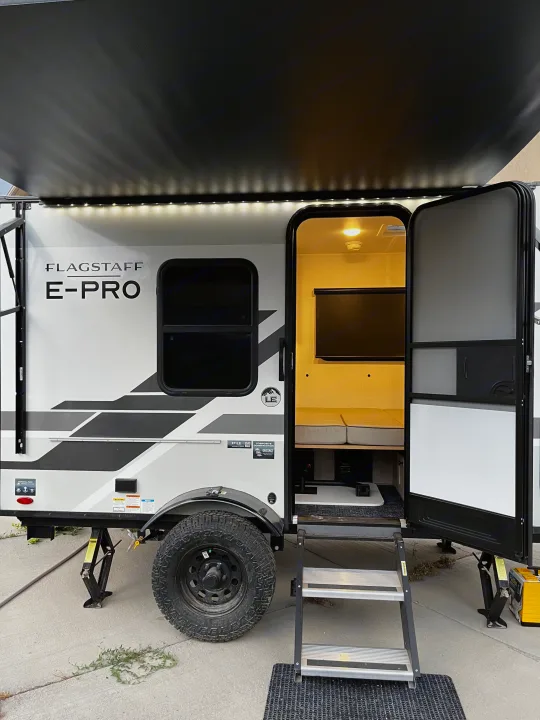 Flagstaff E-Pro RV rental with open door revealing lit interior, extended awning, and rugged tires for camping adventures.. Forest River Flagstaff E-Pro 2026