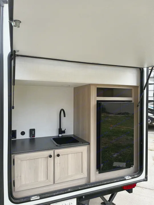 This RV rental's outdoor kitchen features a sink, black faucet, and Magic Chef mini-fridge, perfect for camping convenience.. Forest River Flagstaff E-Pro 2026