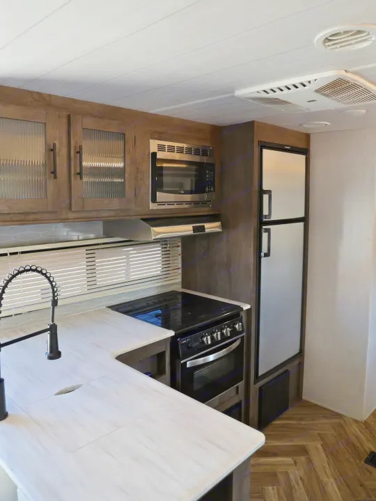 Modern rv rental kitchen with wood cabinets, microwave, fridge, stove, marble-look counters, and herringbone floor.. Forest River Salem Cruise Lite 2022