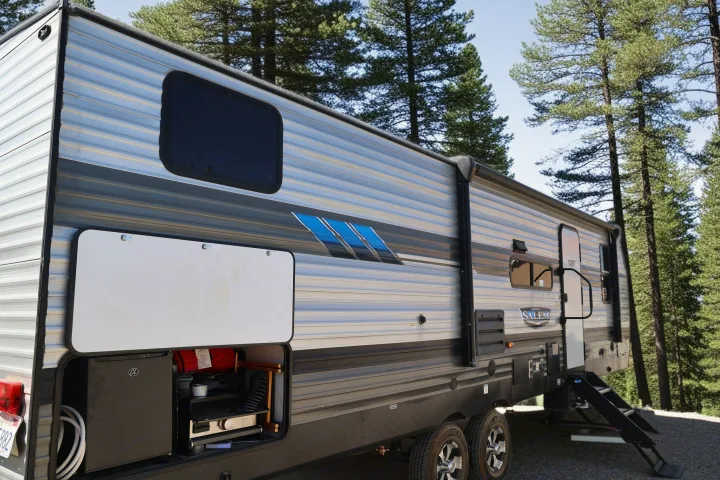 This RV rental travel trailer showcases its convenient outdoor amenities with an open storage compartment revealing a compact fridge and grill, ready for camping.. Forest River Salem Cruise Lite 2022