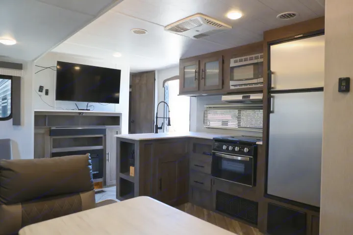 Explore this modern rv rental interior! Features a full kitchen with stove, fridge & sink, plus a living area with TV and fireplace.. Forest River Salem Cruise Lite 2022